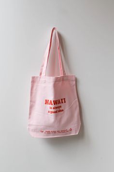 a pink tote bag hanging on a wall with the words hawaii printed on it