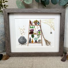 a framed artwork with shells and other items on the shelf in front of a plant