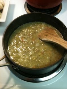 a pot filled with green soup sitting on top of a stove next to a wooden spoon