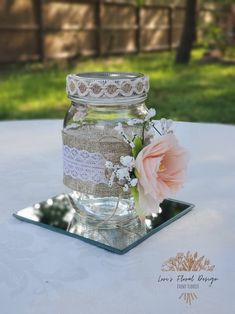 a glass jar sitting on top of a table next to a pink flower and lace