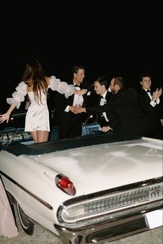 a group of people in tuxedos standing next to a white car at night