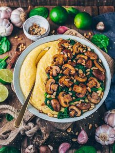 a bowl filled with mushrooms and spinach on top of a wooden table next to garlic,