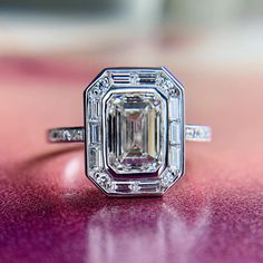 an emerald cut diamond ring sitting on top of a purple surface with diamonds around it