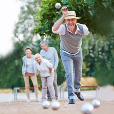 an older man is throwing a ball in the air while three other people watch from behind him