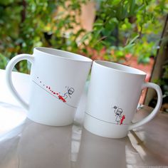 two white coffee mugs sitting on top of a table next to each other,