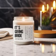 a candle that reads it's giving bride sitting on a table with candles in the background