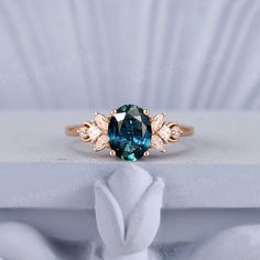 an oval blue and white diamond ring sitting on top of a white cloth covered box