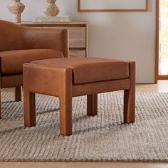 a brown foot stool sitting on top of a rug next to a chair and table