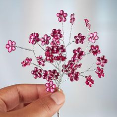 a hand holding a pink flower brooch with tiny flowers on it's side