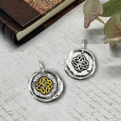 two silver and gold pendants sitting on top of a table next to a book