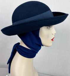 Body is a navy blue felt with the rounded crown and wide curled brim. Attached underneath is a thick blue knit scarf that can be tied in the front or wrapped around the neck and tied in the back. A great hat for winter. Excellent condition with no issues. No size or maker is indicated. Inner circumference is 22 inches. Crown rises 3 1/2 inches and the brim extends 3 inches. Vintage Solid Felt Hat For Winter, Retro Wide Brim Cloche Hat For Winter, Classic Blue Winter Hat, Navy Curved Brim Hat For Winter, Navy Adjustable Hat For Winter, Adjustable Navy Winter Hat, Navy Adjustable Winter Hat, Classic Blue Brimmed Felt Hat, Blue Wool Hat For Winter