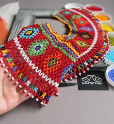 a hand is holding a beaded item near some other beads and paint samples on a table