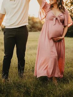 a pregnant woman standing next to a man in a field