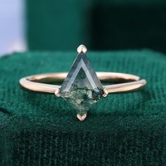 a gold ring with a green tourmaline stone in it sitting on top of a green cloth