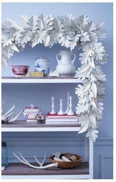 an arrangement of white flowers and vases on top of bookshelves in a room with blue walls