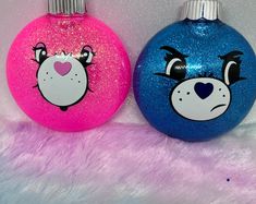 two blue and pink ornaments with faces painted on the front one has a bear's face