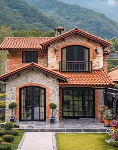 a house that is in the middle of some grass and bushes with mountains in the background