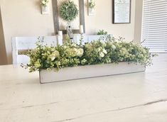 a white table topped with a planter filled with green and white flowers sitting on top of a wooden table