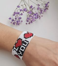 a hand with a beaded bracelet on it next to purple flowers and a plant