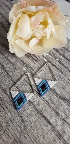 a pair of earrings sitting on top of a wooden table next to a flower and a white rose