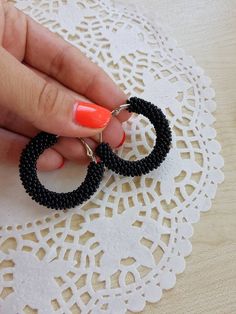 a woman is holding onto some black beaded hoop earrings on a lace doily