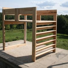 a wooden bed frame sitting on top of a cement slab in the grass next to a field