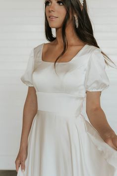 a woman in a white dress is standing with her hands on her hips and looking off to the side