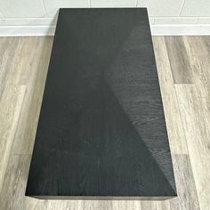 a black table top sitting on the floor in front of a white brick wall and wooden floors