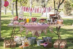 a picnic table with food and drinks on it in the middle of a park area