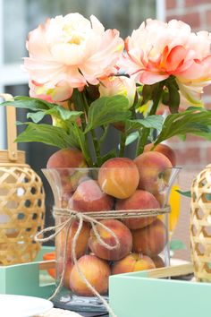 peaches and flowers in a glass vase on a table with other items around it