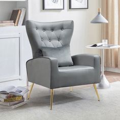 a gray chair sitting in a living room next to a white table and two pictures on the wall