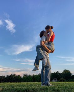 a man holding a woman in his arms while standing on top of a lush green field