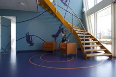 an empty room with blue walls and orange chairs next to a stair case in the center