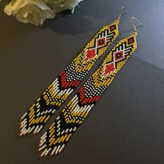 a pair of beaded earrings sitting on top of a table next to a flower