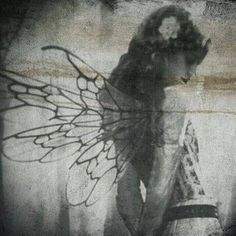 a black and white photo of a woman with wings on her back, standing in front of a wall