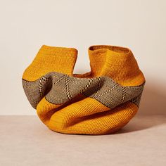 an orange and brown knitted vase sitting on top of a table next to a white wall