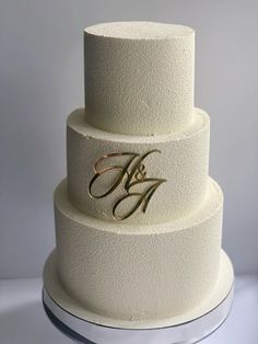 a three tiered white cake with gold lettering