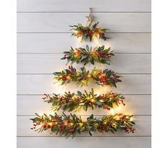 a christmas tree made out of lights and greenery on a white wooden wall with red berries