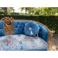 a blue couch sitting in front of a hedge next to a gold framed mirror on top of a wooden table