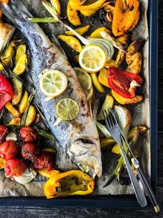 fish and vegetables are on a tray with silverware, lemons, tomatoes, peppers