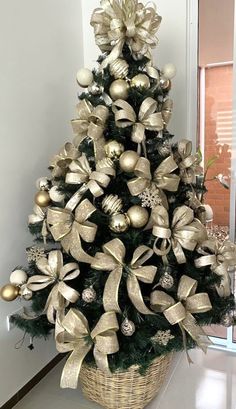 a small christmas tree with gold ornaments in a basket on the floor next to a window