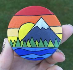 a hand holding a painted rock with mountains in the background