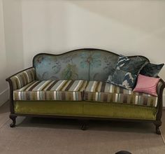 a green couch with striped pillows on it in front of a white wall and floor