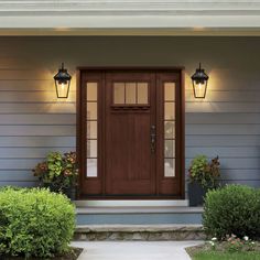 the front door of a house with two lights above it and plants on either side