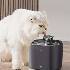 a white cat drinking water out of a black and gray fountain with it's tongue hanging out