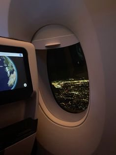 an airplane window with the view of earth through it's screen and city lights in the distance