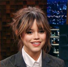 a young woman smiling while wearing a suit and tie in front of a cityscape