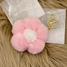 a pink furry ball with a gold keychain on top of it next to a white bag