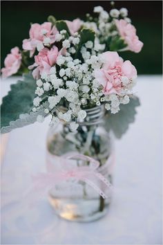 pink and white flowers in a mason jar on a table with ribbon tied around it