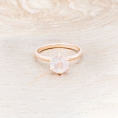 a gold ring with an oval shaped white stone on the center, sitting on top of a wooden surface